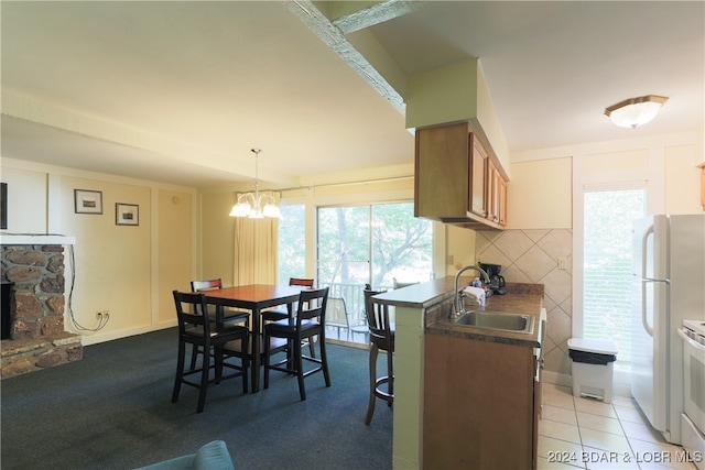 kitchen featuring hanging light fixtures, a stone fireplace, kitchen peninsula, sink, and a chandelier