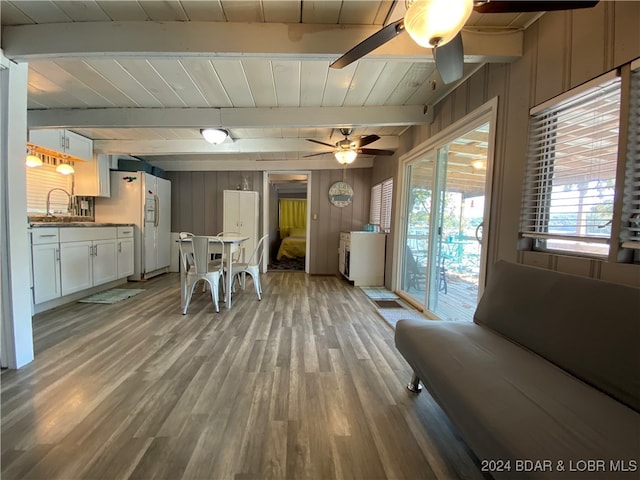 living room featuring wood-type flooring, sink, beam ceiling, wooden walls, and ceiling fan