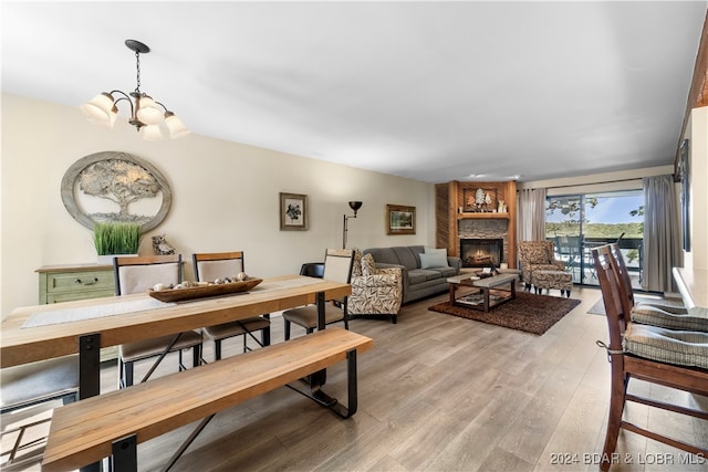 dining room featuring a stone fireplace, a notable chandelier, and light hardwood / wood-style floors