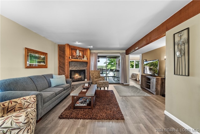 living room featuring wood-type flooring, beamed ceiling, and a stone fireplace