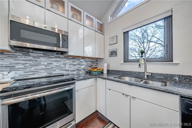 kitchen with appliances with stainless steel finishes, dark stone countertops, vaulted ceiling, white cabinets, and sink