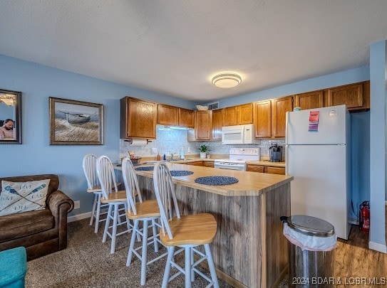 kitchen with decorative backsplash, a breakfast bar, white appliances, dark hardwood / wood-style flooring, and sink