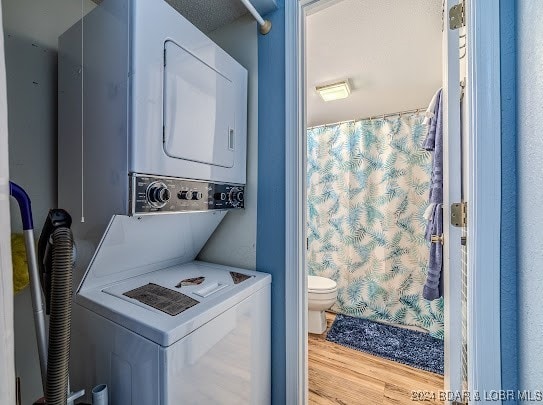 clothes washing area with light hardwood / wood-style floors and stacked washer / drying machine