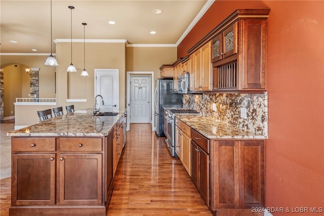 kitchen with light hardwood / wood-style floors, sink, an island with sink, hanging light fixtures, and appliances with stainless steel finishes