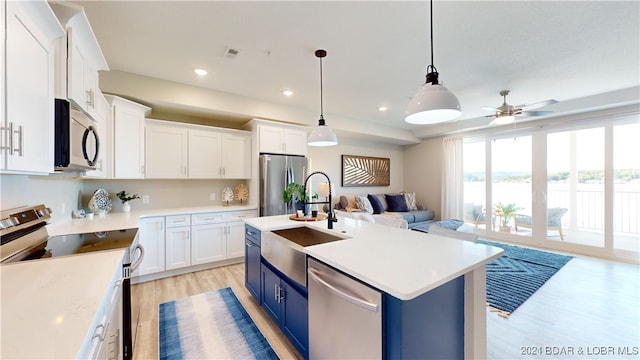 kitchen with white cabinets, a kitchen island with sink, blue cabinetry, appliances with stainless steel finishes, and light hardwood / wood-style floors