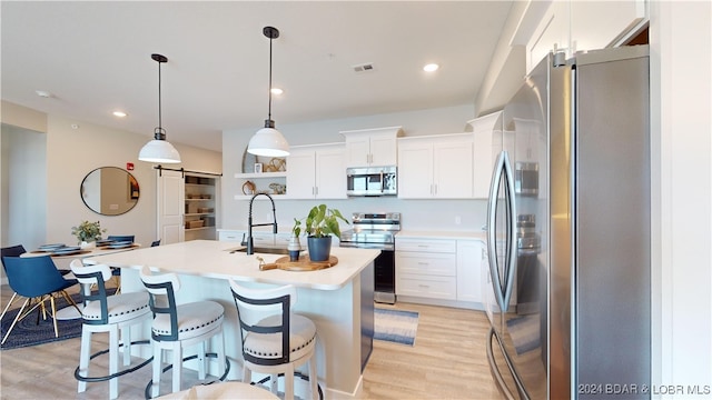 kitchen with decorative light fixtures, stainless steel appliances, a barn door, and white cabinetry