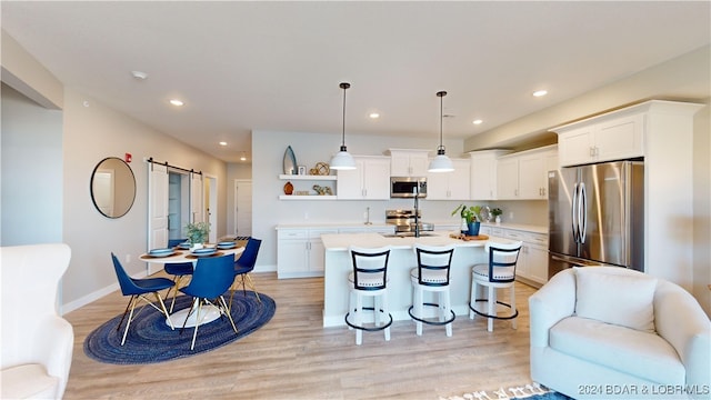 kitchen with an island with sink, hanging light fixtures, white cabinetry, appliances with stainless steel finishes, and a barn door