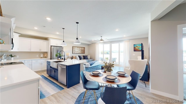 kitchen with blue cabinets, white cabinets, a kitchen island with sink, light hardwood / wood-style flooring, and stainless steel appliances