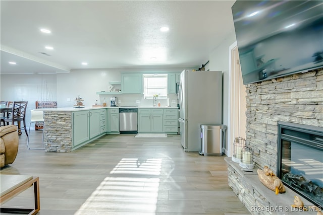 kitchen featuring a stone fireplace, green cabinetry, stainless steel appliances, light wood-type flooring, and sink