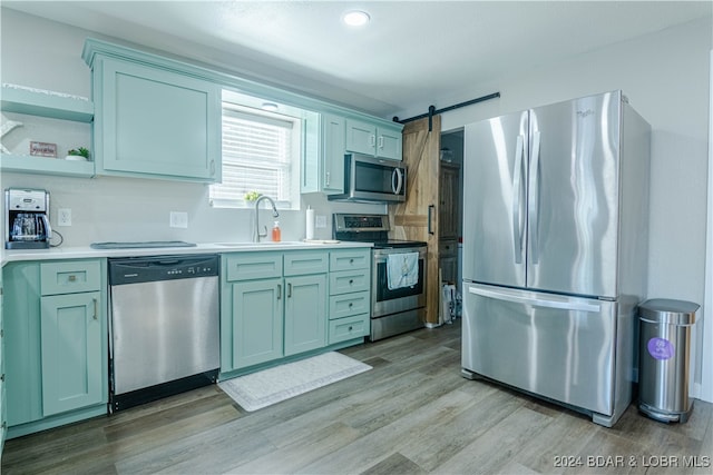 kitchen with light hardwood / wood-style flooring, stainless steel appliances, sink, and a barn door