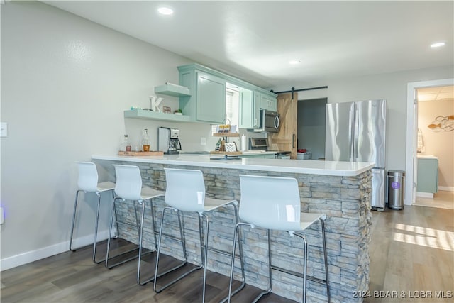 kitchen with appliances with stainless steel finishes, a barn door, kitchen peninsula, a breakfast bar area, and dark hardwood / wood-style floors