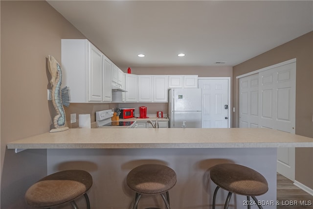 kitchen featuring white cabinets, kitchen peninsula, stainless steel refrigerator, a kitchen breakfast bar, and white stove