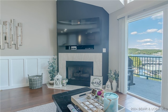 living room with vaulted ceiling, a tiled fireplace, and hardwood / wood-style flooring