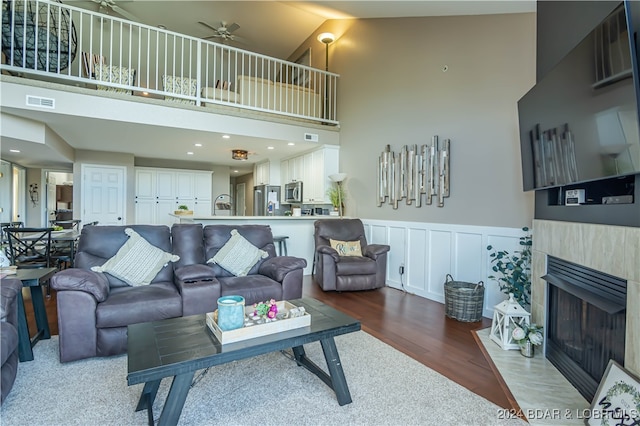 living room featuring ceiling fan, a tiled fireplace, dark hardwood / wood-style flooring, and high vaulted ceiling