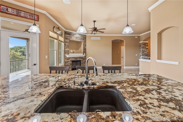 kitchen featuring a stone fireplace, pendant lighting, crown molding, ceiling fan, and sink