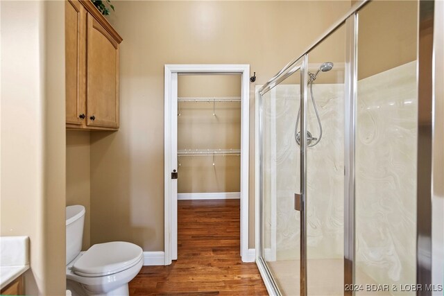 bathroom with hardwood / wood-style flooring, a shower with shower door, and toilet