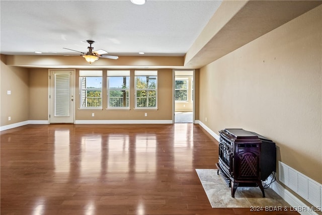 living room with a textured ceiling, ceiling fan, a wood stove, and hardwood / wood-style flooring