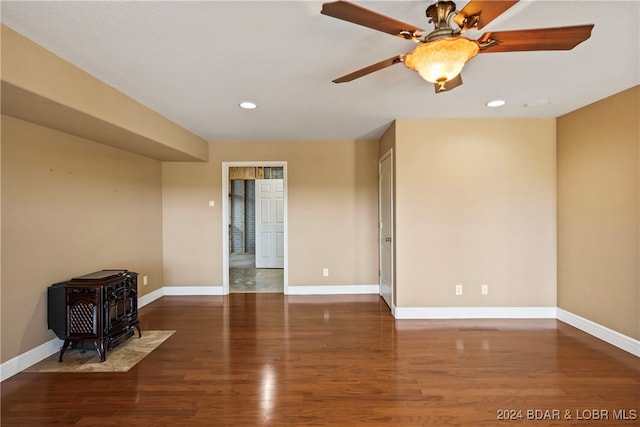 spare room featuring ceiling fan, dark hardwood / wood-style flooring, and a wood stove