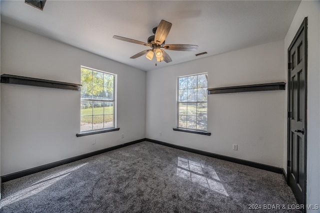 unfurnished bedroom featuring multiple windows, dark carpet, and ceiling fan