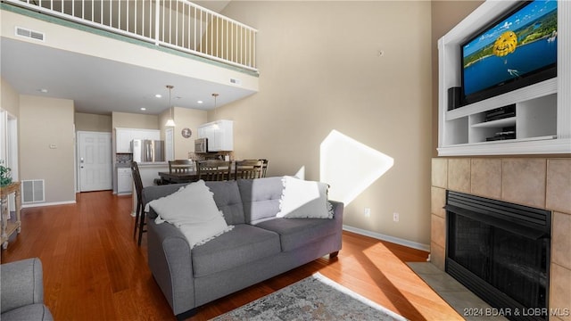 living room with baseboards, visible vents, a tiled fireplace, and wood finished floors