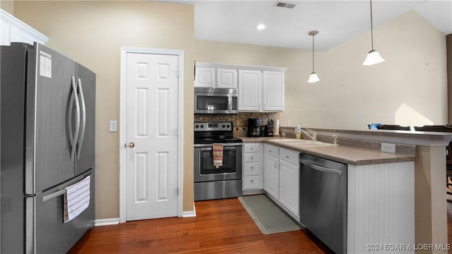 kitchen featuring decorative backsplash, white cabinets, a peninsula, stainless steel appliances, and a sink