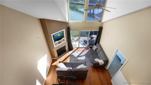 living area with a ceiling fan, a high ceiling, a tiled fireplace, and wood finished floors