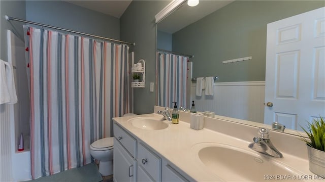 bathroom featuring a wainscoted wall, double vanity, a sink, and toilet