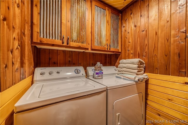 laundry room featuring separate washer and dryer, wooden walls, and cabinets