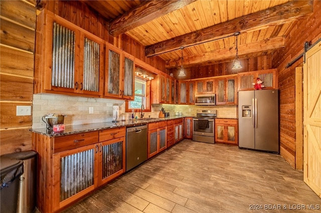 kitchen featuring appliances with stainless steel finishes, wooden walls, a barn door, decorative light fixtures, and dark stone countertops