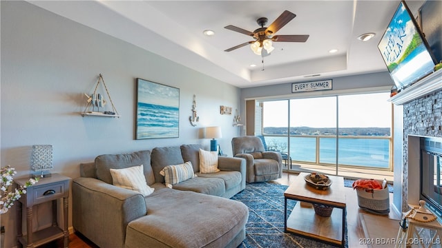 living room with a water view, ceiling fan, and a tray ceiling