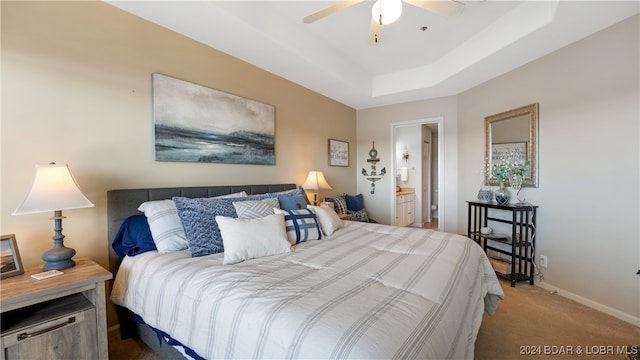 carpeted bedroom featuring ceiling fan, a raised ceiling, and ensuite bathroom