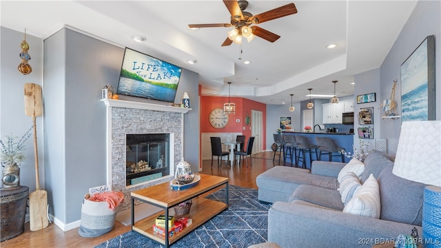 living room with a tray ceiling, ceiling fan, dark hardwood / wood-style floors, and a fireplace