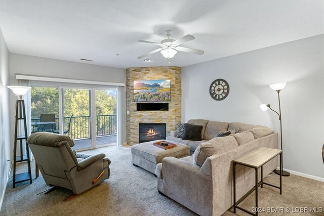 carpeted living room featuring ceiling fan and a stone fireplace