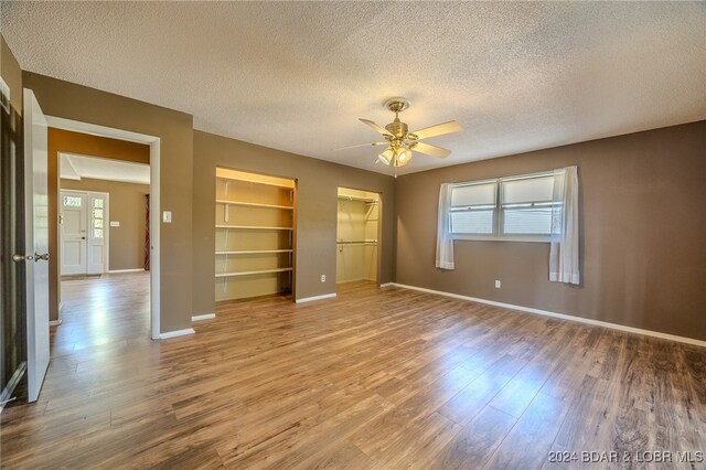 unfurnished bedroom with light hardwood / wood-style flooring, a textured ceiling, a walk in closet, and ceiling fan