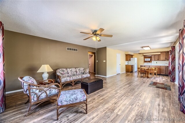 living room featuring light hardwood / wood-style flooring, ceiling fan, and a textured ceiling