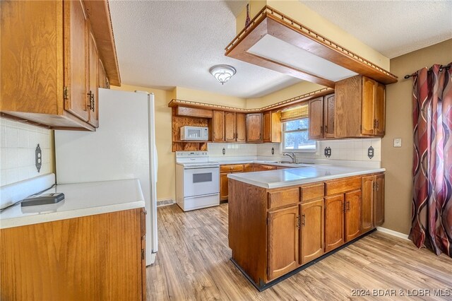 kitchen featuring a textured ceiling, light hardwood / wood-style flooring, tasteful backsplash, and white appliances