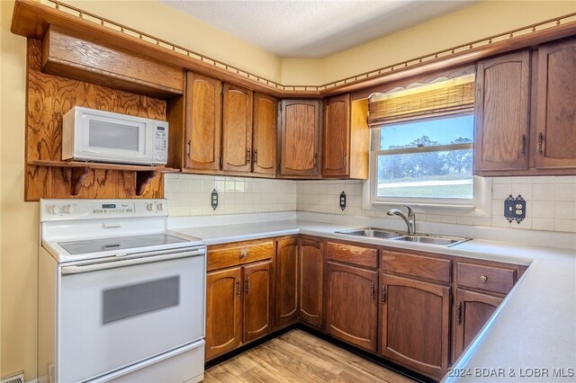 kitchen with light wood-type flooring, a textured ceiling, sink, backsplash, and white appliances