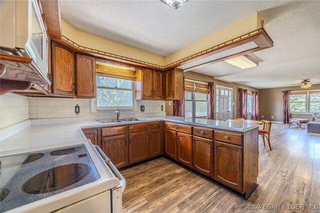 kitchen with light hardwood / wood-style floors, backsplash, kitchen peninsula, white stove, and sink