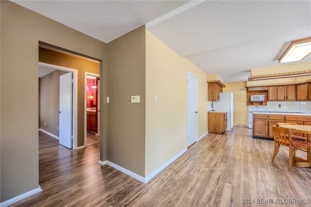 kitchen featuring a textured ceiling, backsplash, white appliances, and hardwood / wood-style floors