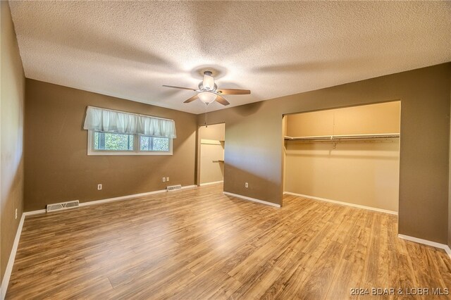 unfurnished bedroom featuring a closet, ceiling fan, light wood-type flooring, and a textured ceiling