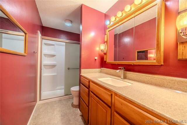 bathroom featuring a textured ceiling, vanity, toilet, and a shower with shower door