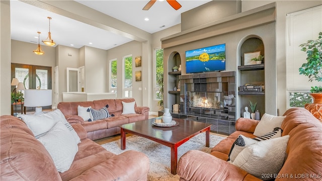 living room with a tiled fireplace, built in features, and ceiling fan