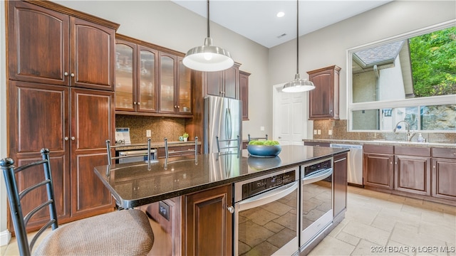 kitchen with dark stone counters, a center island, tasteful backsplash, stainless steel appliances, and decorative light fixtures