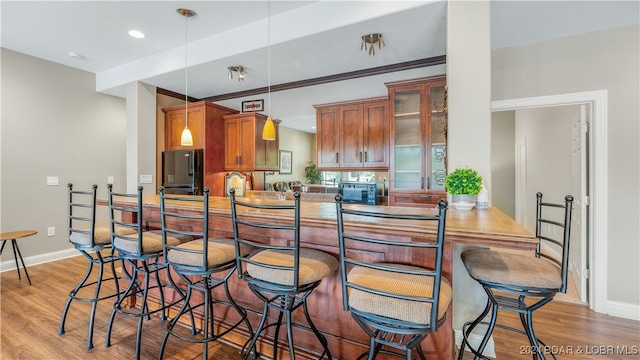 kitchen featuring fridge, hanging light fixtures, kitchen peninsula, and light hardwood / wood-style flooring