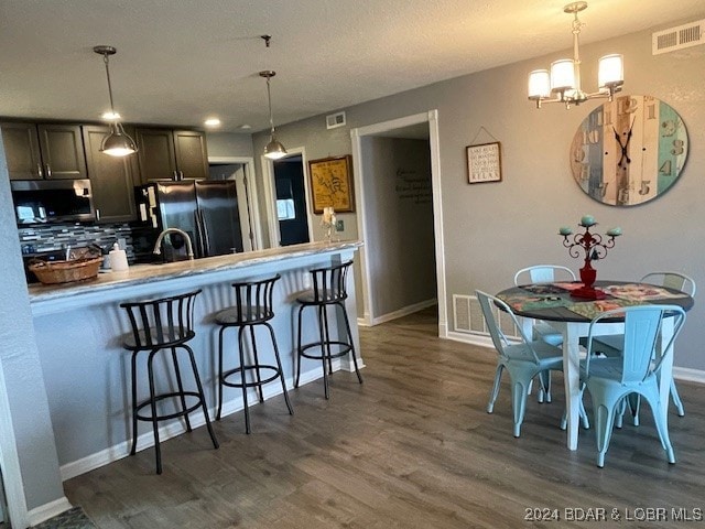 kitchen with tasteful backsplash, a kitchen bar, decorative light fixtures, dark hardwood / wood-style flooring, and black refrigerator