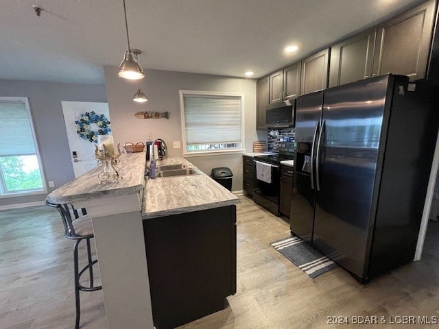 kitchen with a breakfast bar, sink, hanging light fixtures, light hardwood / wood-style flooring, and black appliances