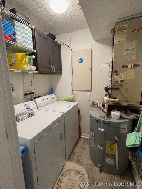 clothes washing area featuring independent washer and dryer, electric water heater, light wood-type flooring, a textured ceiling, and cabinets