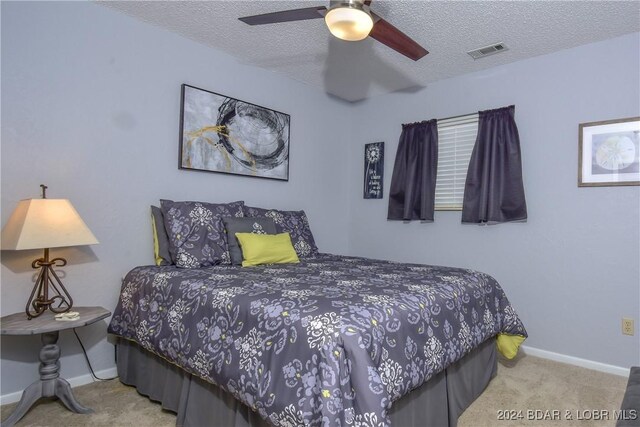 bedroom with ceiling fan, light colored carpet, and a textured ceiling