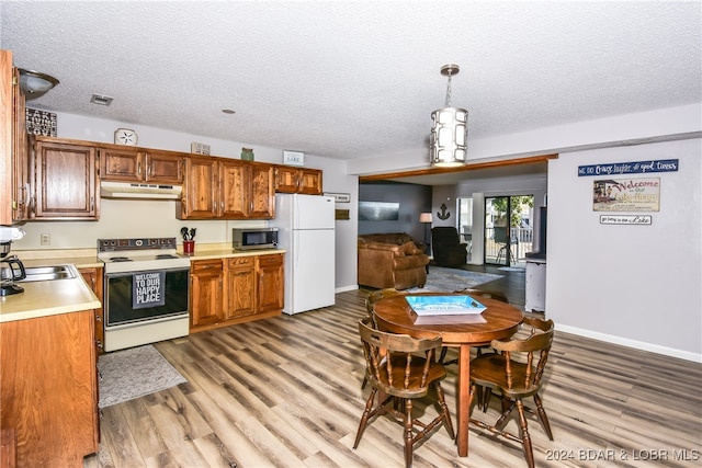 kitchen featuring white appliances, light hardwood / wood-style floors, decorative light fixtures, and a textured ceiling