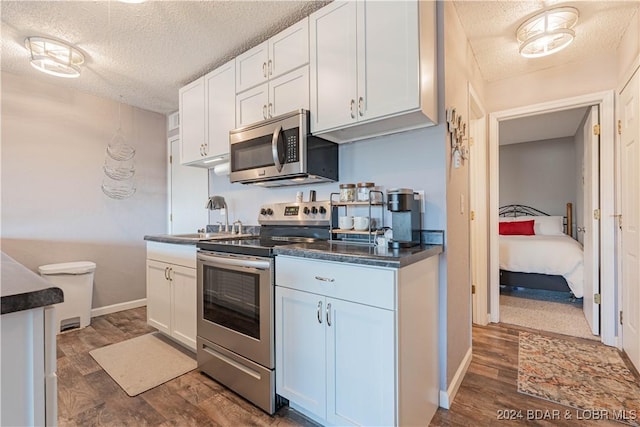 kitchen with a textured ceiling, dark wood-type flooring, white cabinets, and appliances with stainless steel finishes